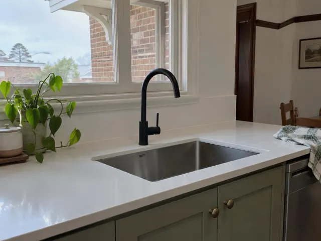 Black gooseneck kitchen mixer tap over a stainless sink with white benchtop and window in Hexham
