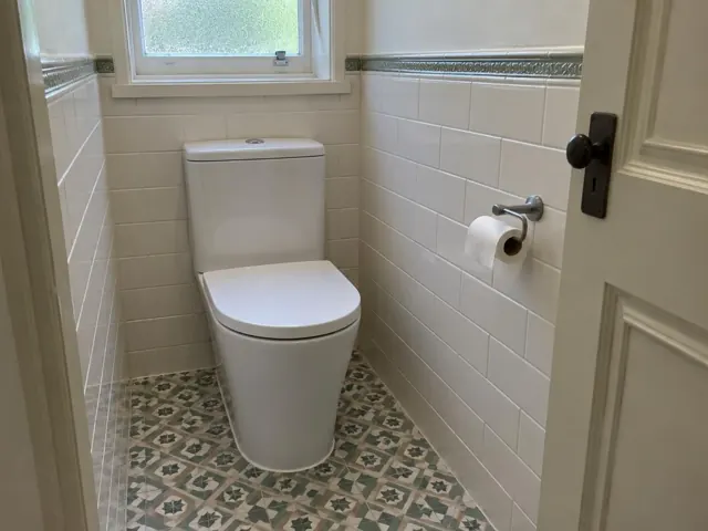 White toilet in a tiled narrow bathroom with patterned floor and window in Wallsend